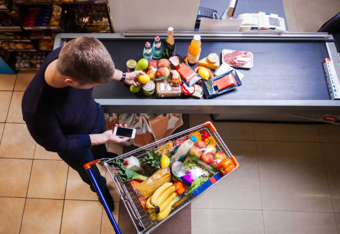 Young man putting goods on counter in supermarket